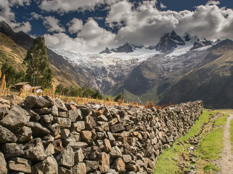 Blick auf die Anden mit Steinmauer und Hütte im Vordergrund.
