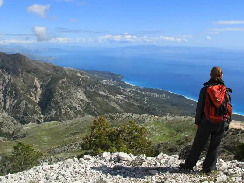 Wanderer auf einem Berggipfel mit Blick auf die Küste und das türkisblaue Meer.