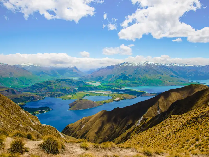 Panoramablick von einem Berg auf eine Seenlandschaft mit schneebedeckten Bergen im Hintergrund.