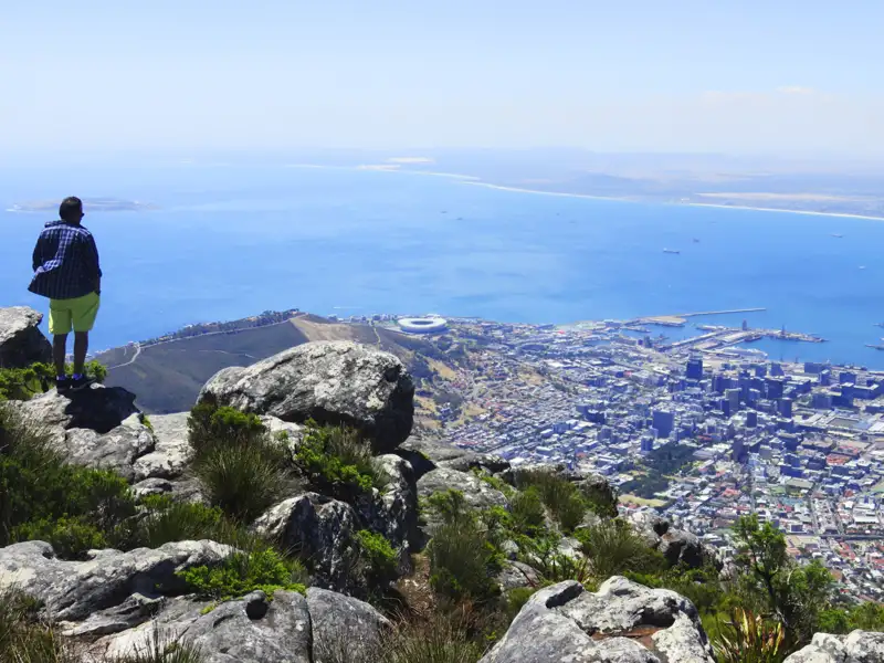 Panoramablick auf Kapstadt vom Tafelberg. Der Reisende steht auf felsigem Gelände und betrachtet die Stadt und das Meer.