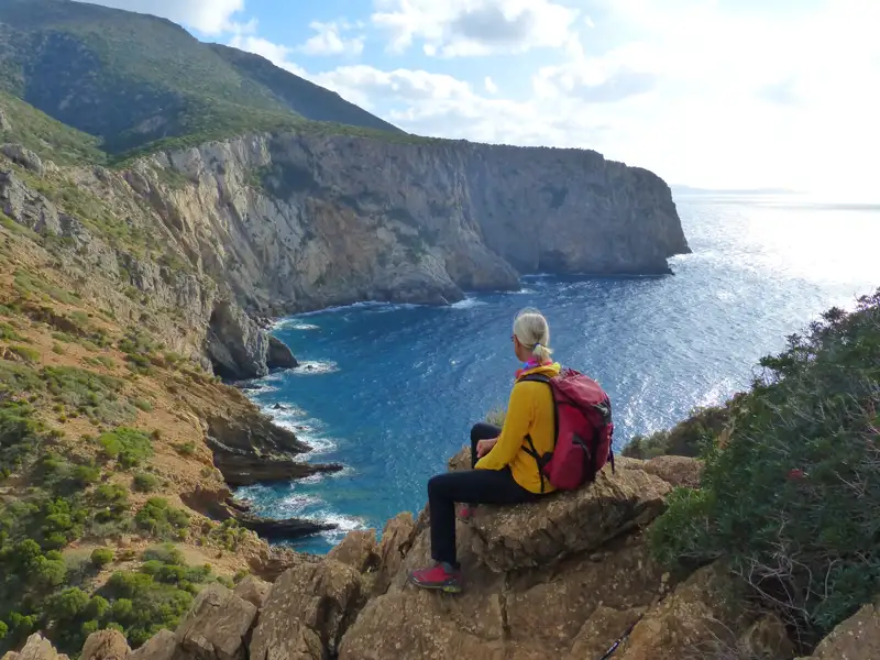 Wanderer pausiert auf einem Felsen und betrachtet die Küste.