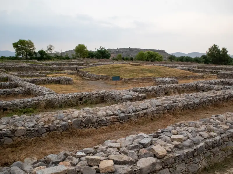 Steinmauern und Hügel einer Ausgrabungsstätte.