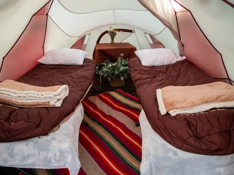Zwei Betten in einem Zelt, ausgestattet mit Decken und Kissen, bereit für die Nacht.