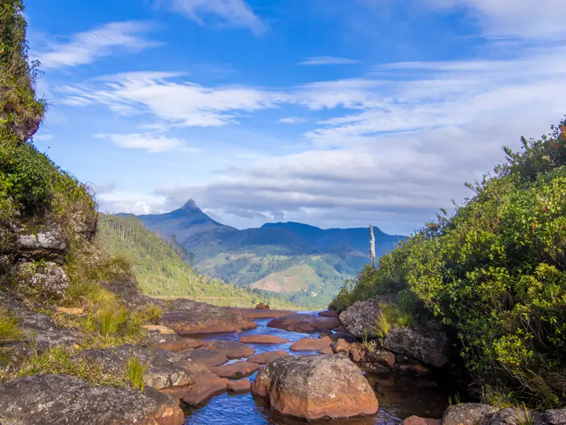 Felsiger Bachlauf mit Blick auf einen Berggipfel.