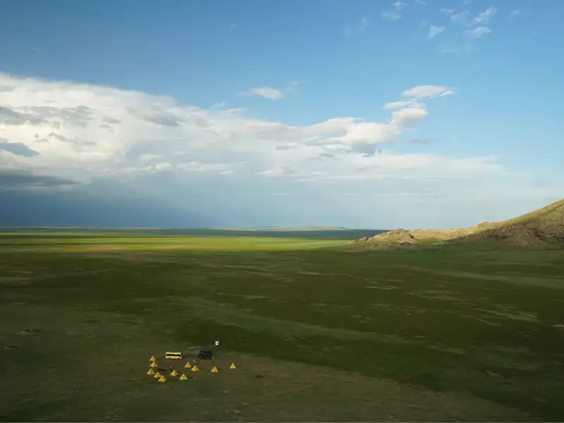 Ein Zeltlager in einer weiten grünen Ebene mit einem Bus, der auf die Reise hinweist.