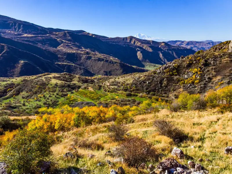 Herbstliche Berglandschaft mit Tal und Blick auf einen schneebedeckten Gipfel.