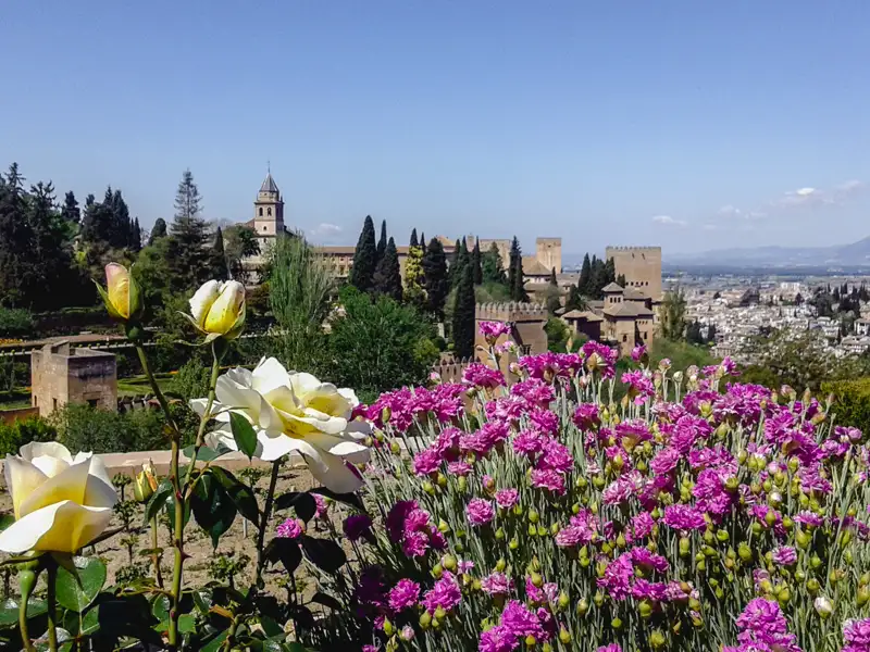 Blick auf die Alhambra von den Gärten aus, mit bunten Blumen im Vordergrund.