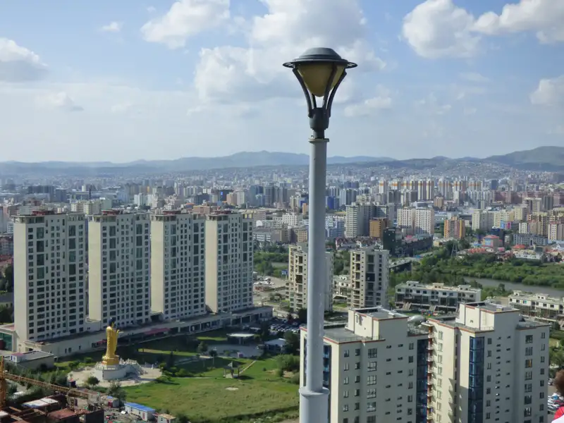 Ausblick über die Stadt mit modernen Wohngebäuden und einer goldenen Statue, möglicherweise ein religiöses Denkmal.
