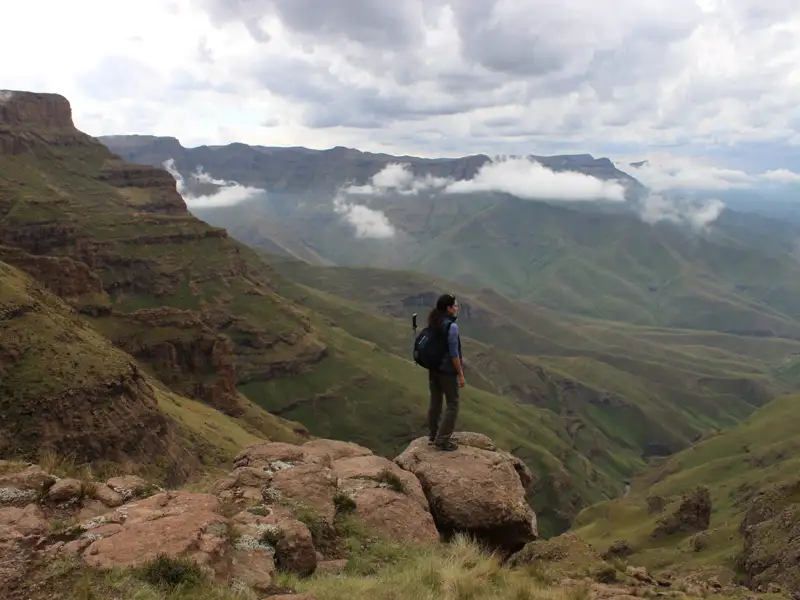 Wanderer auf einem Felsvorsprung mit Blick auf das bergige Gelände.
