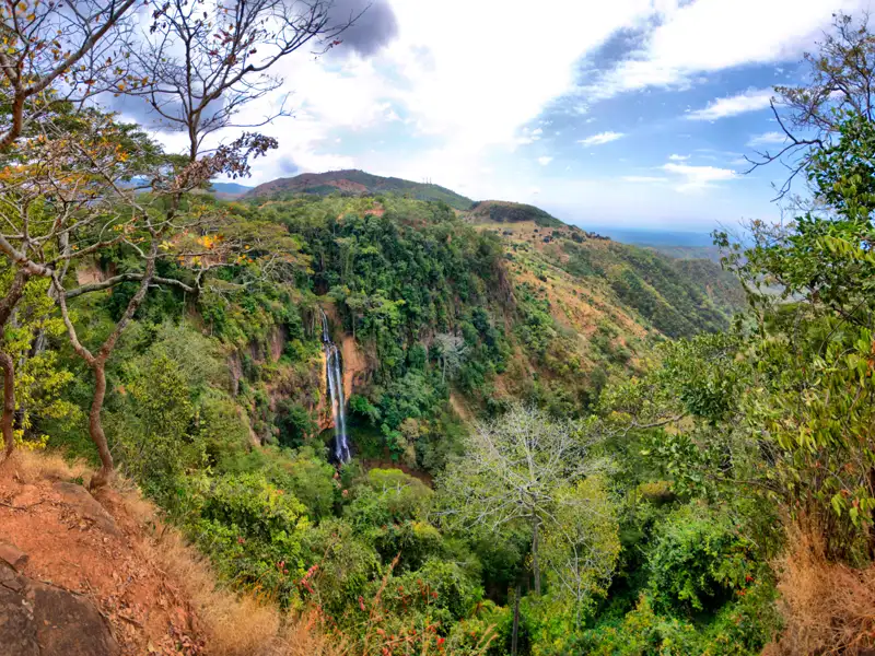 Panoramablick auf einen Wasserfall inmitten einer üppigen grünen Landschaft.