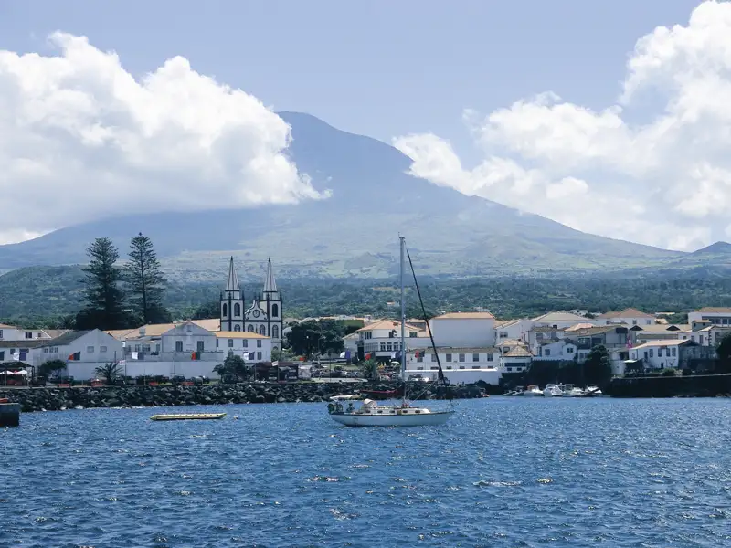 Blick auf eine Küstenstadt mit weißer Kirche und einem Vulkan im Hintergrund.