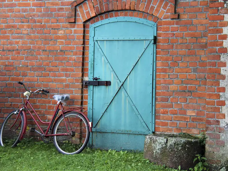 Rotes Fahrrad vor türkisfarbener Tür und roter Backsteinmauer.