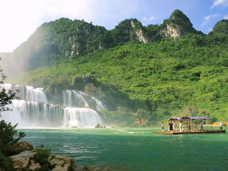 Besucher auf einem Floß vor einem Wasserfall.