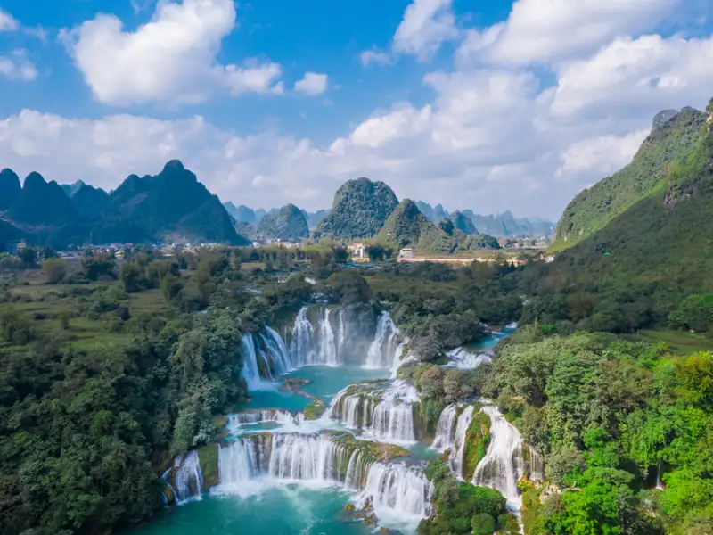 Mehrstufiger Wasserfall in einer grünen, hügeligen Landschaft.