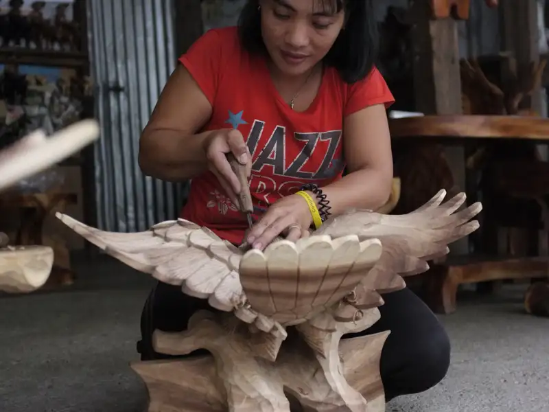 Kunsthandwerkerin beim Schnitzen einer Adler-Skulptur aus Holz.