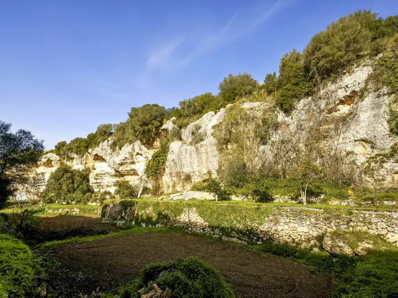 Felsige Landschaft mit Bäumen und Sträuchern sowie landwirtschaftlich genutzten Flächen im Vordergrund.