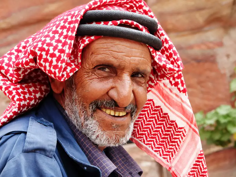 Ein älterer Mann mit einem traditionellen rot-weißen Kopftuch und einem freundlichen Lächeln.