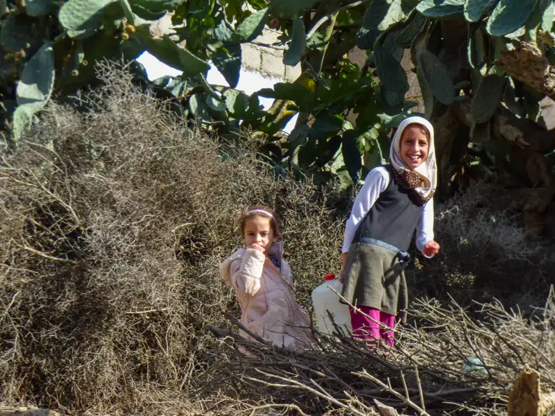 Zwei Mädchen stehen in einer Landschaft mit trockenen Ästen und einem Kaktus, ein Hinweis auf die lokalen Gegebenheiten.