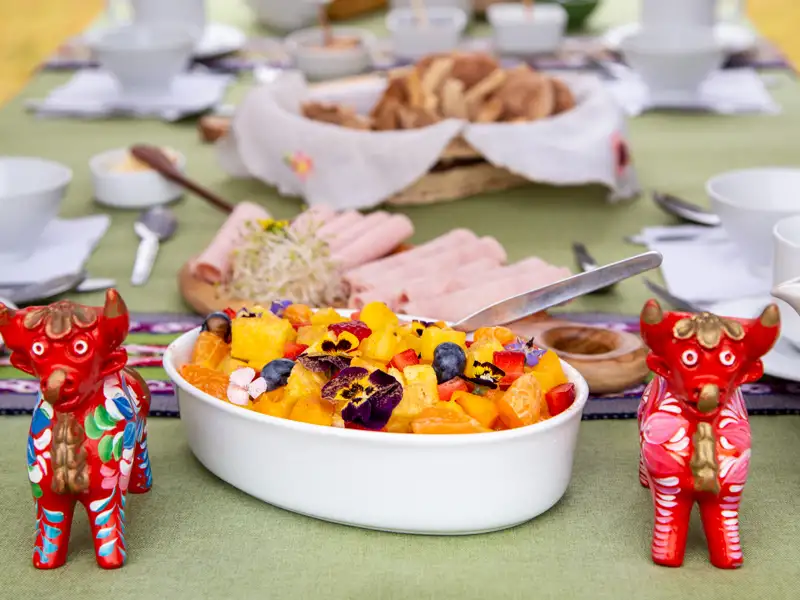 Obstsalat auf einem Frühstückstisch mit Brot und Aufschnitt.