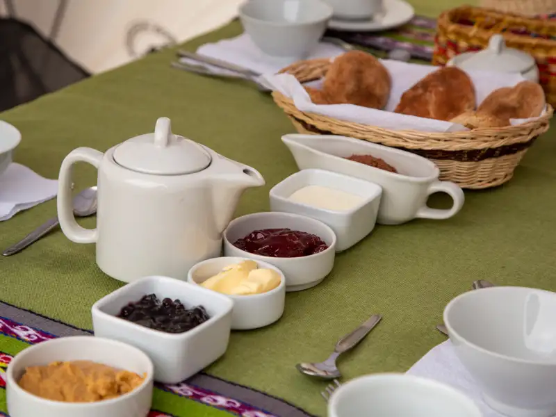 Frühstückstisch mit Teekanne, Brötchenkorb, Marmelade, Butter, Sahne und Schokocreme.