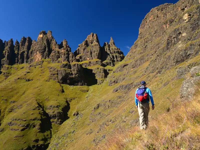 Wanderer auf einem Bergpfad mit Blick auf Felsformationen.