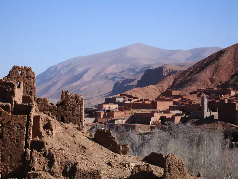 Traditionelle Lehmziegelgebäude und Ruinen einer Siedlung in einer Berglandschaft.