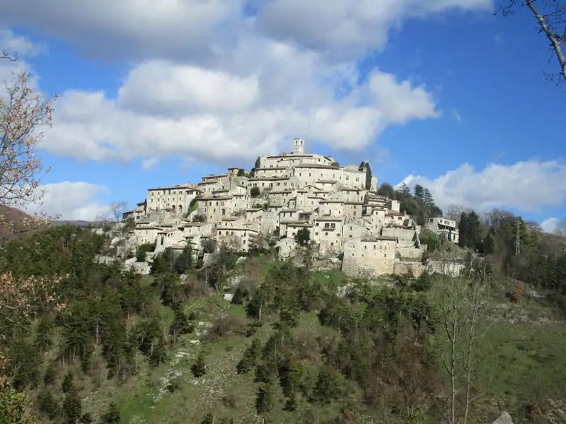 Panoramablick auf ein italienisches Bergdorf, umgeben von bewaldeten Hügeln.