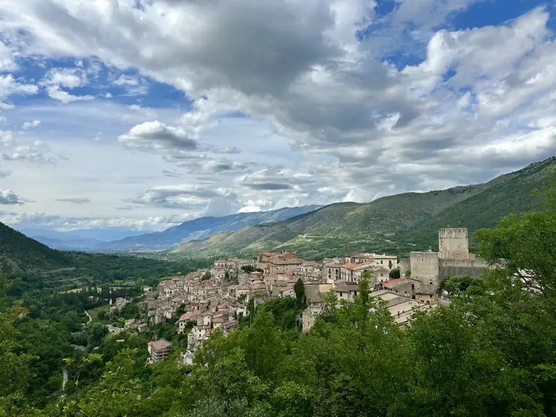 Panoramablick auf ein italienisches Bergdorf mit umliegenden Bergen und Bäumen.