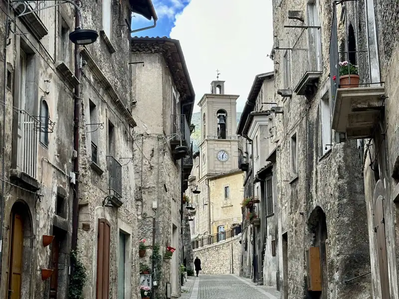 Enge Straße in einem italienischen Dorf mit Blick auf einen Kirchturm.