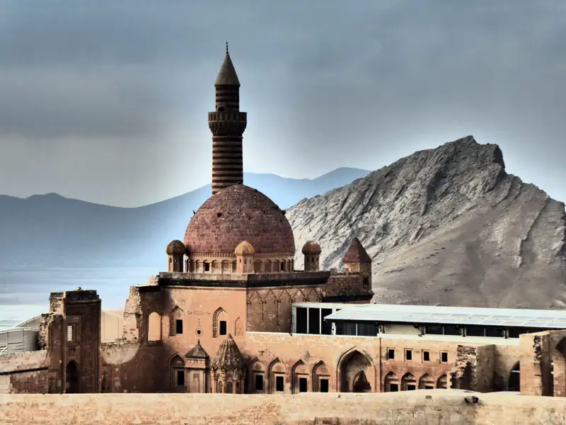 Historische Gebäude und ein Minarett vor einem Berg.