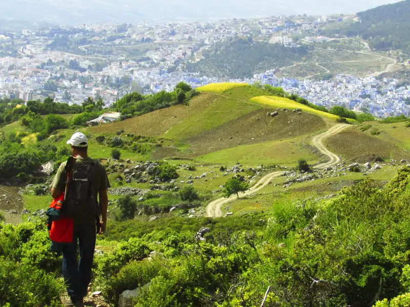 Wanderer auf einem Bergpfad mit Blick auf eine Stadt mit blauen Gebäuden.