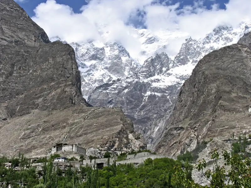 Bergdorf mit schneebedeckten Gipfeln im Hintergrund.