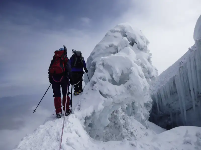 Zwei Bergsteiger besteigen einen verschneiten Berggrat mit Eisformationen.