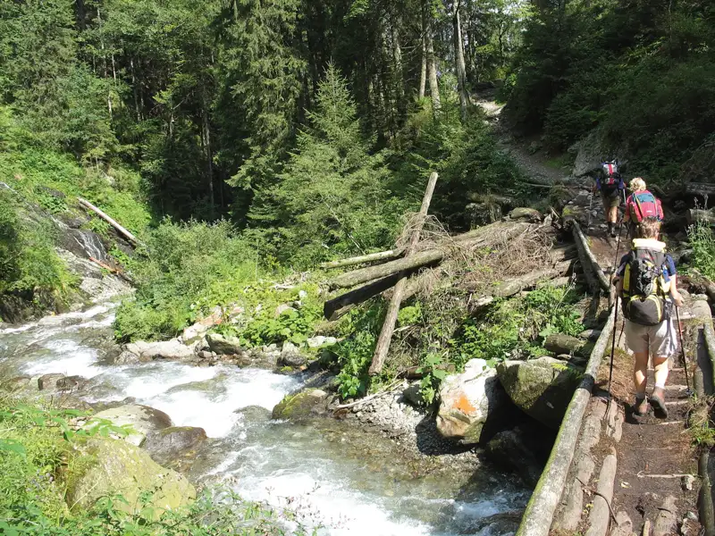 Wanderer auf einem improvisierten Holzsteg über einen Bach im Wald.