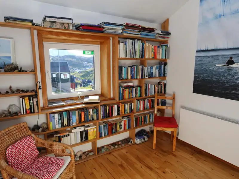 Blick in die Leseecke der Unterkunft. Bücherregale und ein Sessel laden zum Verweilen ein. Das Fenster bietet einen Blick auf die umliegende Landschaft.