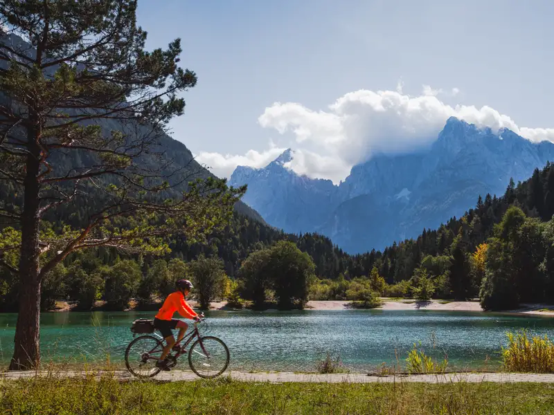 Radfahrer auf einer Tour entlang eines Bergsees mit Blick auf die Bergkette.