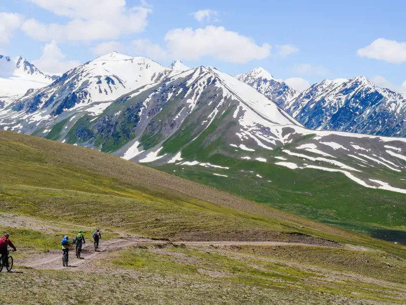 Mountainbiker auf einem Bergpfad mit schneebedeckten Bergen im Hintergrund.
