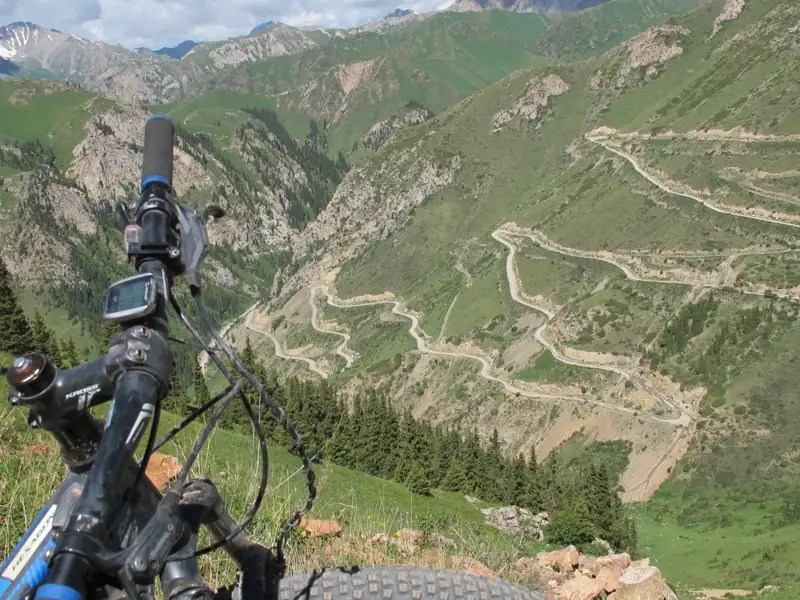 Blick vom Mountainbike-Lenker auf eine kurvenreiche Bergstraße.