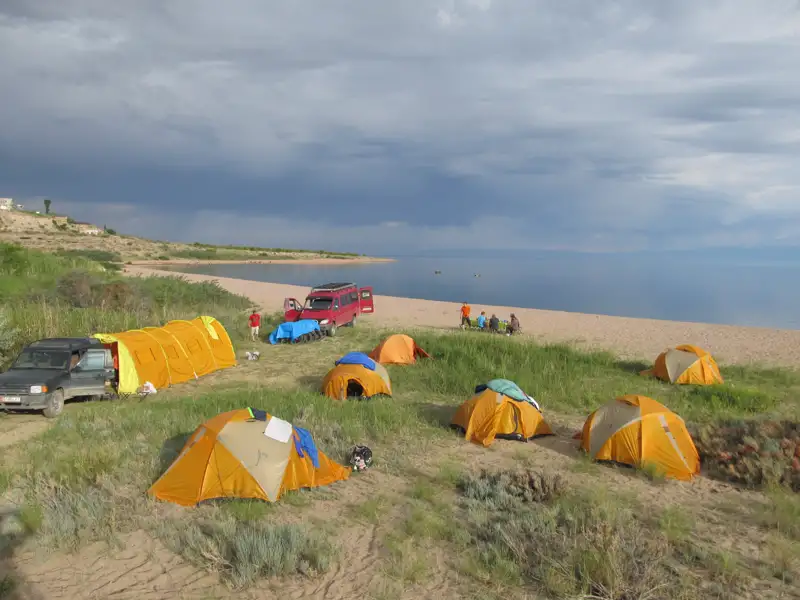 Zeltplatz am Seeufer mit Fahrzeugen und Personen.