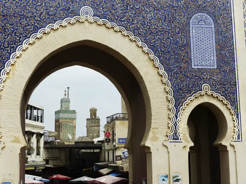 Blick durch ein verziertes Tor in Fes auf die dahinterliegende Moschee und den Markt.