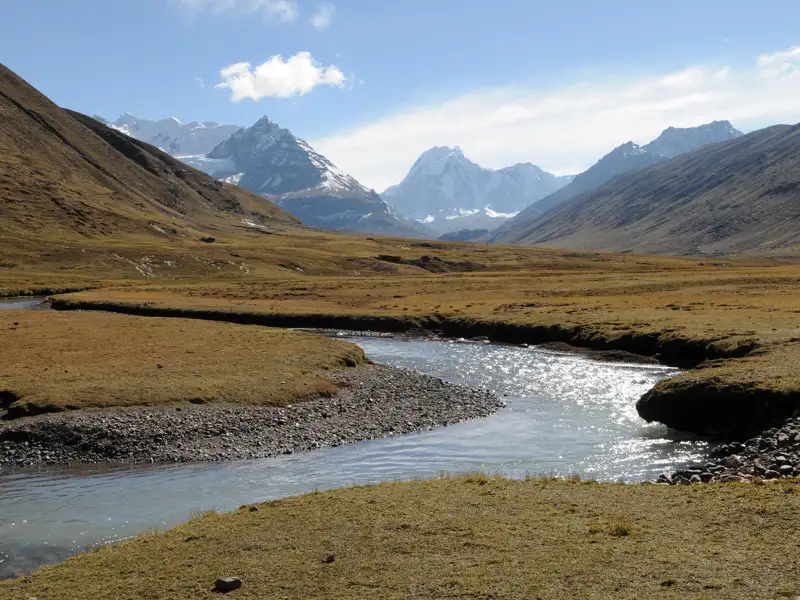 Flusslandschaft in den Bergen mit schneebedeckten Gipfeln im Hintergrund.
