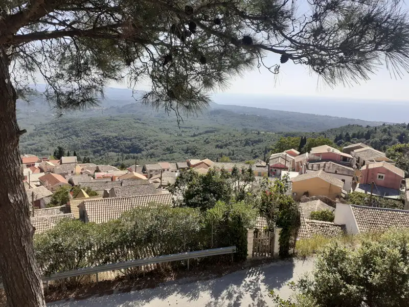 Blick über die Dächer eines Dorfes in Richtung der bewaldeten Hügel und des Meeres.