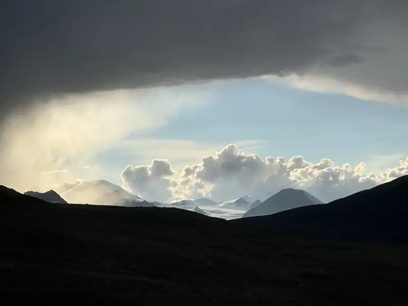 Schneebedeckte Berglandschaft mit dramatischen Wolken und Regenschauer.