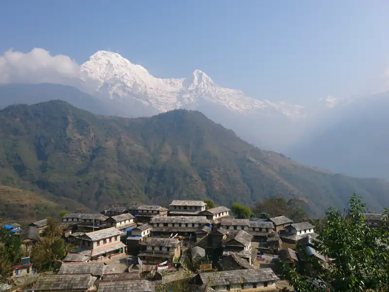 Panoramablick auf ein traditionelles nepalesisches Bergdorf mit den majestätischen schneebedeckten Gipfeln des Himalayas im Hintergrund.