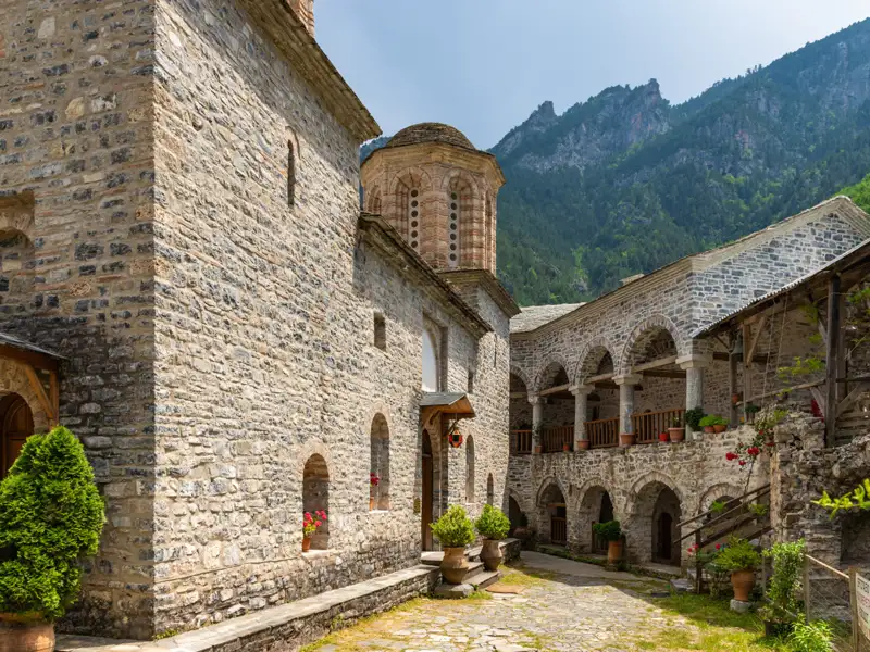 Steingebäude und Innenhof eines Klosters mit Bergkulisse.