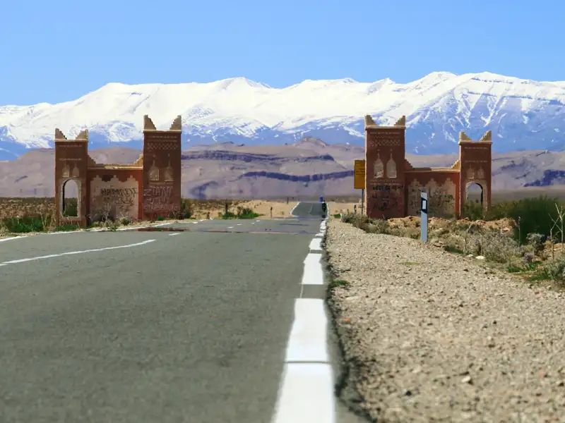 Straßenszene mit Torbogen und schneebedeckten Bergen im Hintergrund.