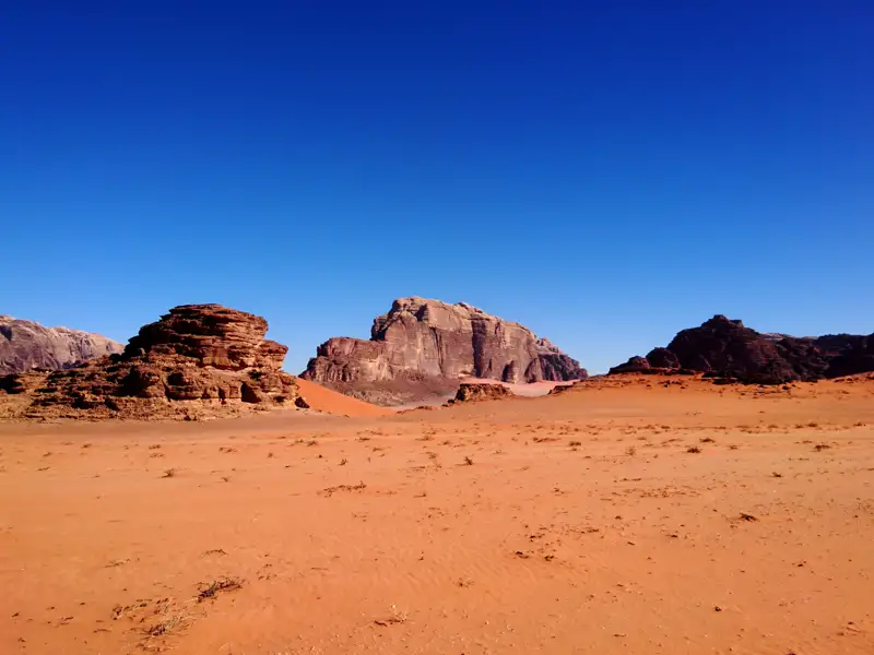 Sanddünen und Felsformationen in der Wüste unter blauem Himmel.