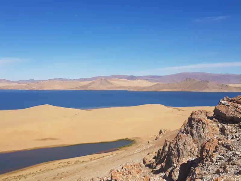 Panoramablick auf einen See, umgeben von Sanddünen und Bergen.
