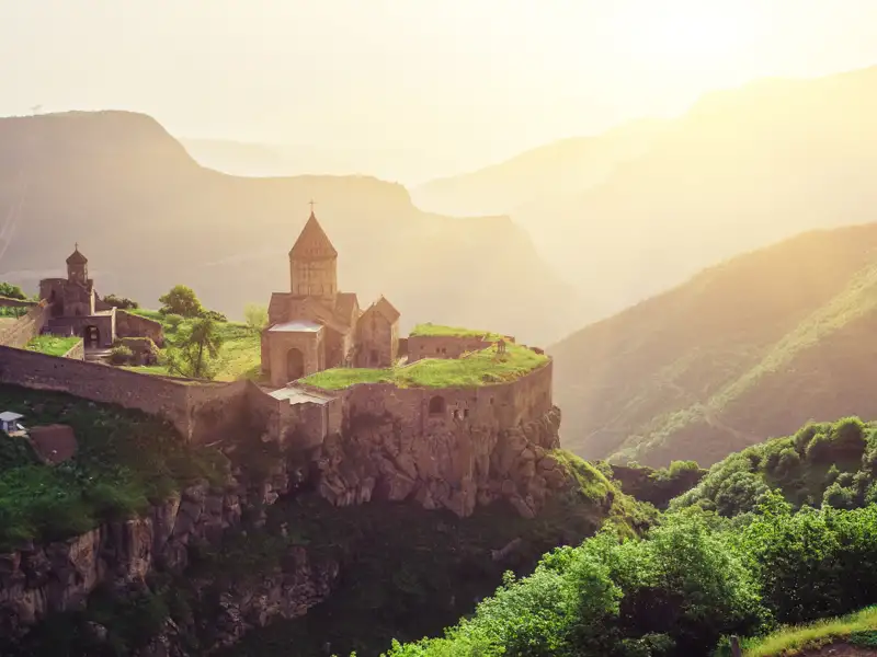 Historische Klosteranlage in bergiger Landschaft bei Sonnenuntergang.