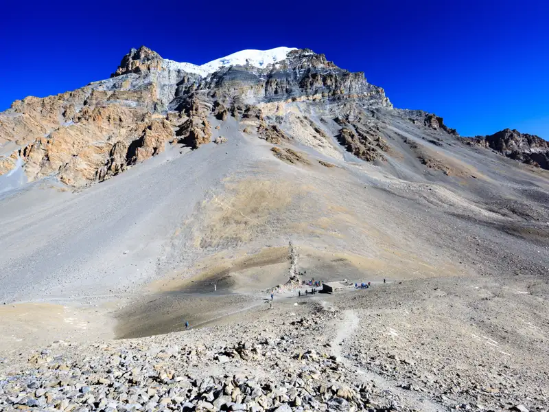 Schneebedeckter Berggipfel und Wanderer auf einem steinigen Pfad.